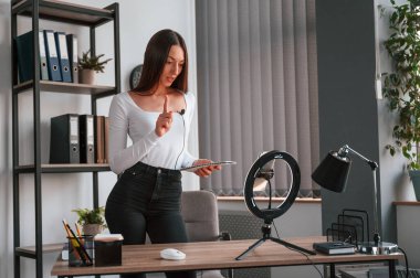 Akıllı telefon kürsüde, kaydediyor. Beyaz elbiseli genç ve güzel bayan ofiste..