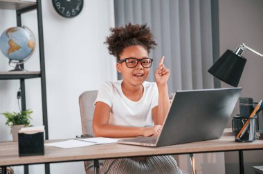 Bir fikrim var, parmağını kaldır. Şirin Afrikalı Amerikalı kız öğrenci dizüstü bilgisayarın yanında oturuyor..