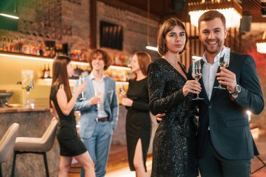 Çift poz veriyor. Güzel giyinmiş bir grup insan içeride yeni yılı kutluyorlar..