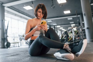 Akıllı telefon kullanıyor. İnce vücutlu spor elbiseli kadın spor salonunda..