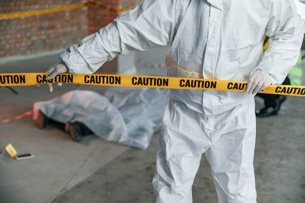 Держу кассету с предупреждением. Детективы собирают улики на месте преступления рядом с трупом.