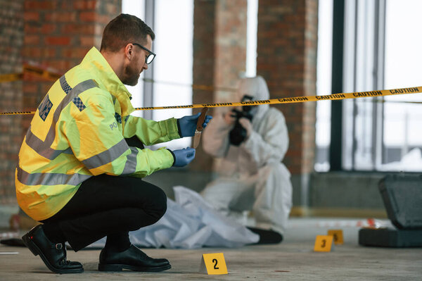 Женщина использует камеру, делает фотографии. Детективы собирают улики на месте преступления рядом с трупом.