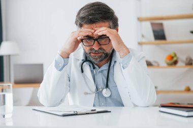 Adam yorgun, başı ağrıyor. Ofiste beyaz önlüklü profesyonel bir sağlık görevlisi var..