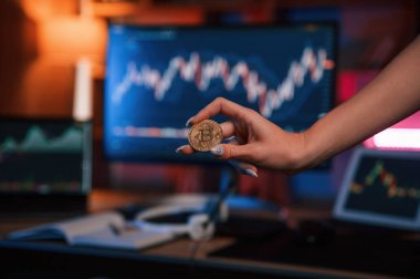 Bitcoin 'i bilgisayar ekranına ve tablete karşı grafiklerle tutan kadının elini kapat.