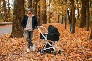 Doğanın tadını çıkarıyorum. Bebek arabalı adam sonbahar parkında yürüyüş yapıyor..