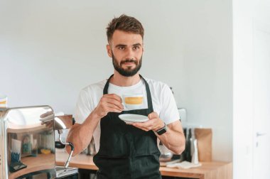 Bir fincan lezzetli kahveyle. Beyaz gömlekli ve siyah önlüklü kafe çalışanı içeride..