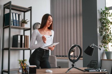 Akıllı telefon kürsüde, kaydediyor. Beyaz elbiseli genç ve güzel bayan ofiste..