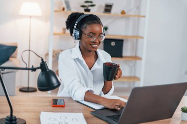 Evden çalışıyorum. Beyaz gömlekli Afrikalı Amerikalı genç bir kadın..