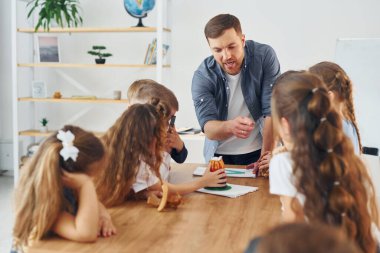 Küçük volkan modeline bakıyorum. Okulda öğretmenle birlikte bir grup çocuk öğrenci..