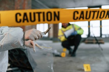 Kadın kovandan kolları tutuyor ve çantaya koyuyor. Dedektifler cesedin yanındaki suç mahallinde kanıt topluyorlar..