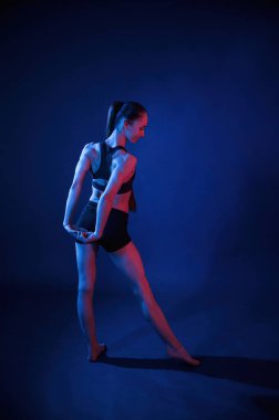 Arkadan bak. Gerinme egzersizlerini ısıt. Güzel kaslı kadın stüdyoda neon ışıklı..