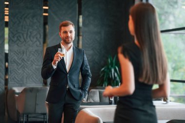 Takım elbiseli adam partide siyah elbiseli bir kadınla konuşuyor..