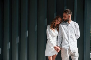 Ayakta durmak ve el ele tutuşmak. Güzel genç çift koyu yeşil arka planda yan yana duruyor..