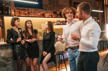 İki erkek eğleniyor. Güzel giyinmiş bir grup insan içeride yeni yılı kutluyorlar..