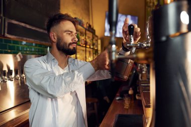 Yan görüş. Barmen bira doldurur. Adam barda çalışıyor..