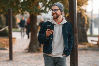 Akıllı telefonla dikiliyorum. Kalın elbiseli güzel adam dışarıda, parkta..