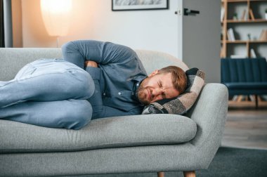 Adamın midesi ağrıyor. Evdeki kanepede uzanmak..