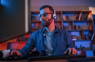 Yoğunlaşmış adam evde bir bilgisayarın başında oturuyor. Neon ışıkları.