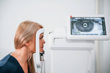 Kadın klinikte oturuyor ve özel bir cihazla görüşünü kontrol ediyor..