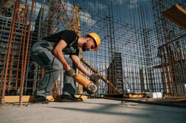 Metal parçaları kesmek için öğütme makinesi kullanıyor. Üniformalı adam inşaat alanında çalışıyor..