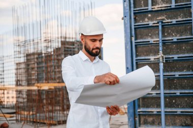 Planı okuyorum. Üniformalı adam inşaat alanında çalışıyor..