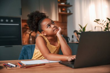 Çizim yapmak için dizüstü bilgisayar ve kağıtla masada oturuyordum. Gündüz vakti evde rahat giyinen sevimli siyah kız var..