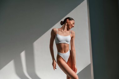 Güneş ışığıyla aydınlatılmış. İnce vücutlu, beyaz bir kadın stüdyoda..