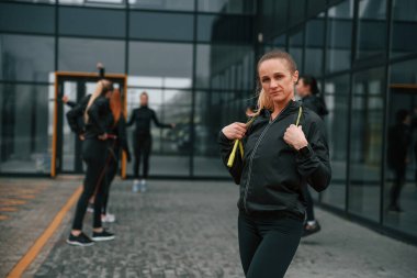 Bir grup sportif kadın dışarıda, siyah binanın yakınında..