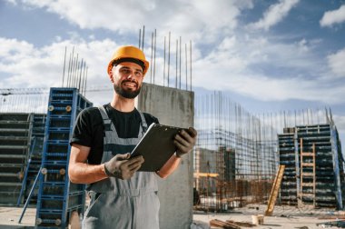Sürecin kontrolü. Foreman belgelerle birlikte. Üniformalı adam inşaat alanında çalışıyor..