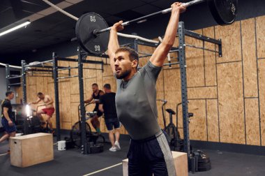 Ellerin havada durarak. Güçlü adam spor salonunda halteri kaldırıyor..