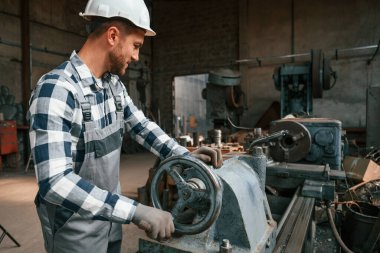 Yan görüş. Makineyi kullanarak. Üniformalı fabrika çalışanı içeride..