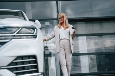 Binanın önünde dikilip içki içiyoruz. Beyaz elbiseli kadın araba galerisinde..