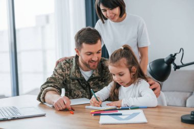 Yeni şeyler öğrenmek ve ödev yapmak. Üniformalı asker karısı ve kızıyla birlikte evde..