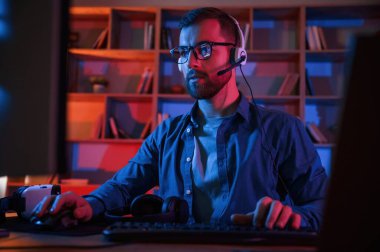 Ön manzara. Evdeki bilgisayar başında oturan bir adam. Neon ışıkları.