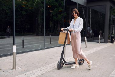 Güneş gözlüklü. Güzel, genç bir bayan dışarıda motosikletiyle bekliyor..