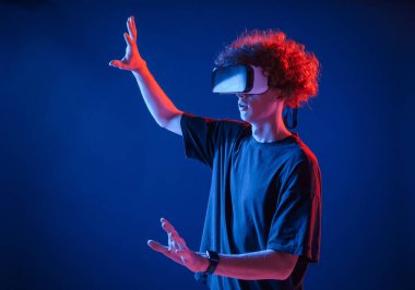 Kıvırcık saçlı genç adam kapalı alanda neon ışıkla aydınlatılır..