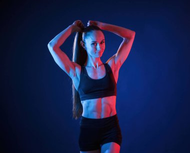 Saçını düzeltiyor. Güzel kaslı kadın stüdyoda neon ışıklı..