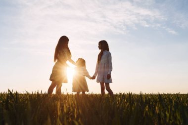 Anne ve iki kızı yazın güneşin doğuşunda tarlada duruyorlar..