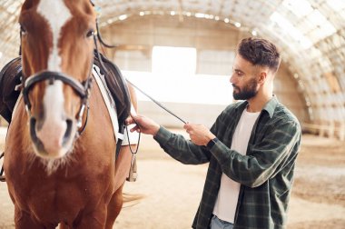 Hayvanı gezintiye hazırlama süreci. Atlı genç adam hangarda..