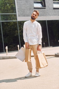 Modern binanın yanında duruyor. Şık genç adamın alışveriş günü var. Çantalarla dışarıda..