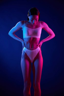Vücudu gösteriyor. İç çamaşırlı genç kadın stüdyoda neon ışıklarıyla bekliyor..