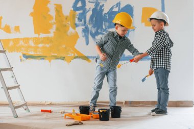 Mavi ve sarı arka plan. İki çocuk ev odasında duvar boyuyor..