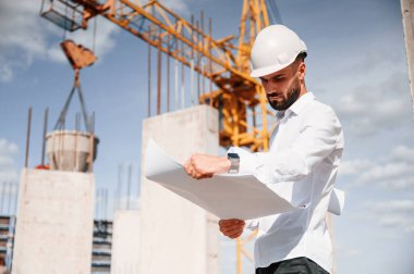 Planı ellerindeyken. Üniformalı adam inşaat alanında çalışıyor..