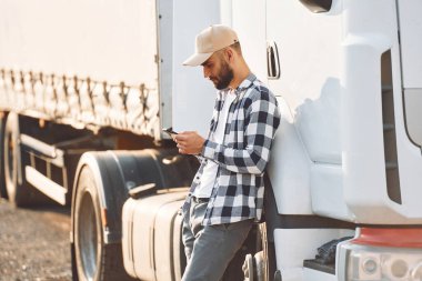 Ayakta ve akıllı telefonu tutarak. Genç kamyon şoförü gündüz vakti aracıyla geliyor..