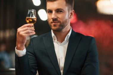 Siyah takım elbiseli zarif bir adam barda alkollü içeceği tadıyor..