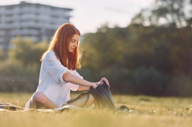 Ekose kumaşın üzerinde çantasıyla oturuyordu. Genç kız güneşli bir günde sahada güzel bir hafta sonu geçiriyor..