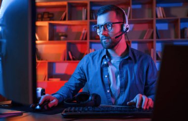 Yoğunlaşmış adam evde bir bilgisayarın başında oturuyor. Neon ışıkları.