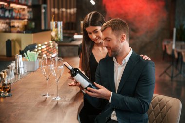 Şarap şişesiyle. Kadın ve erkek barda oturmuş içki içiyorlar..