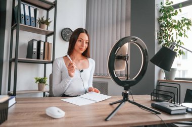 Profesyonel ışıklandırma. Çevrimiçi ana sınıf. Beyaz elbiseli genç ve güzel bayan ofiste..