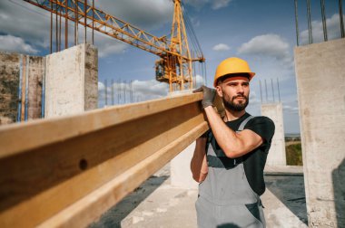 Üniformalı bir adamın inşaat sahasında ahşap bir kalas tutuşu..